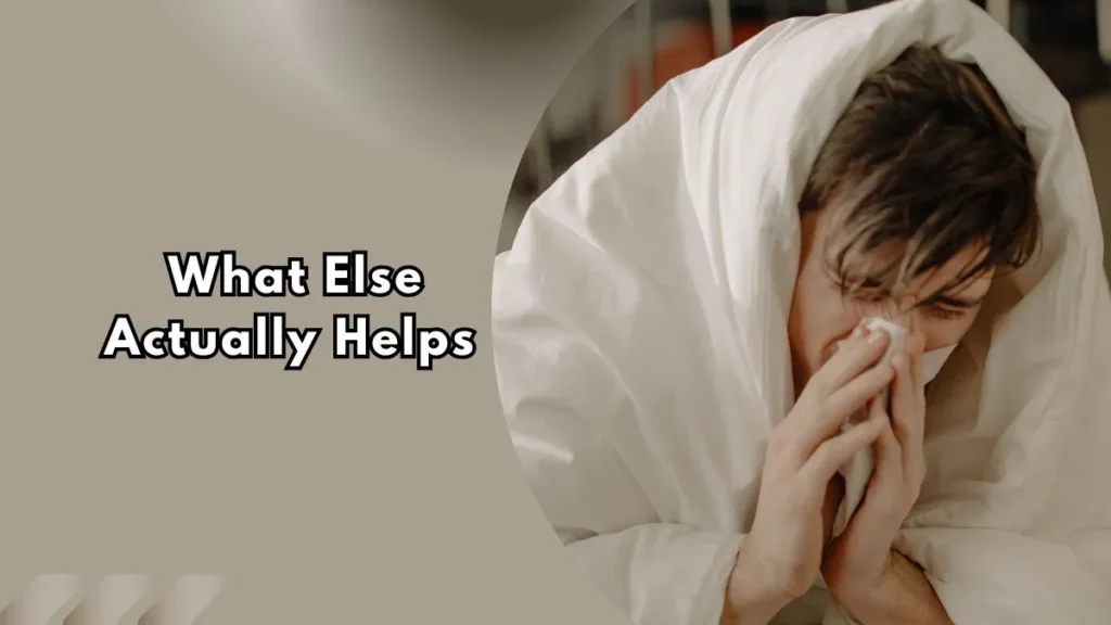 What-Else-Actually-Helps Person with flu symptoms sneezing into a tissue while resting under a blanket